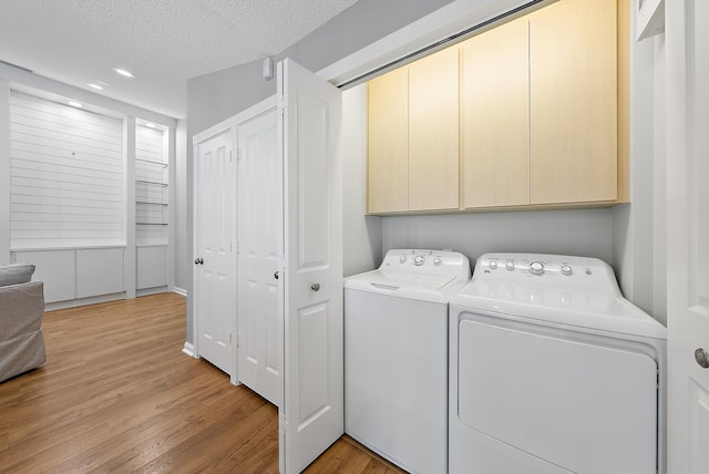 clothes washing area with cabinet space, washer and dryer, a textured ceiling, and light wood-type flooring