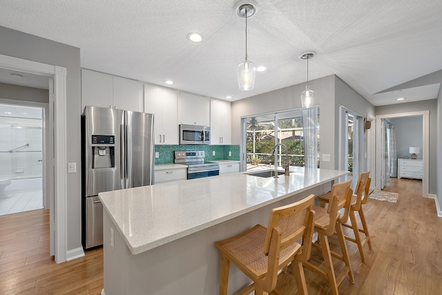 kitchen featuring a kitchen bar, a sink, appliances with stainless steel finishes, white cabinets, and light wood finished floors