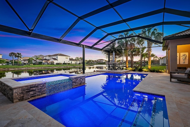 pool at dusk with glass enclosure, a water view, an in ground hot tub, and a patio