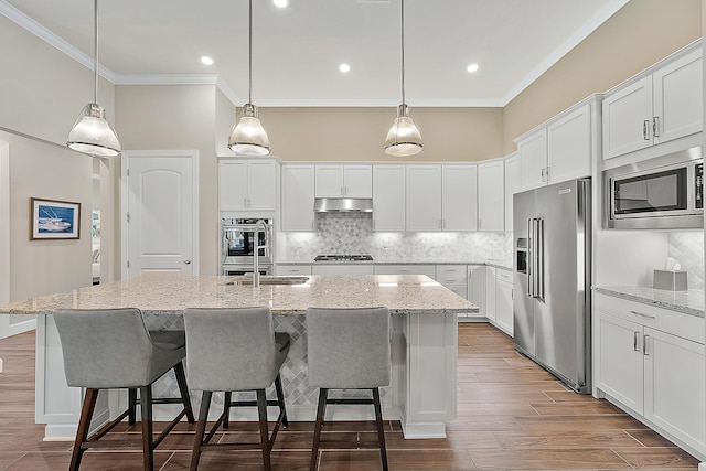 kitchen featuring light stone countertops, appliances with stainless steel finishes, a center island with sink, and white cabinetry