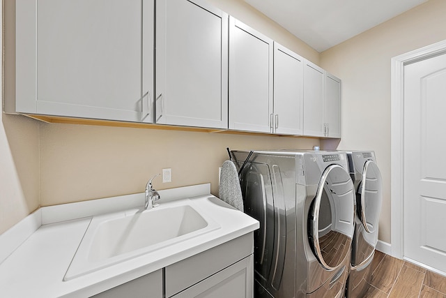 clothes washing area with cabinets, washing machine and dryer, hardwood / wood-style flooring, and sink