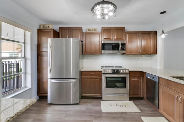 kitchen featuring light stone countertops, hanging light fixtures, backsplash, hardwood / wood-style floors, and appliances with stainless steel finishes