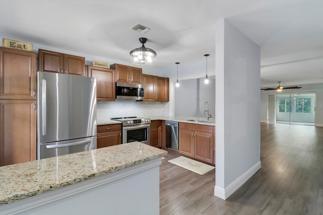 kitchen with light stone countertops, sink, dark hardwood / wood-style floors, pendant lighting, and appliances with stainless steel finishes