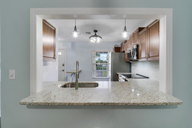 kitchen with light stone countertops, sink, hanging light fixtures, and appliances with stainless steel finishes