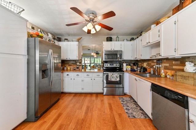 kitchen with sink, white cabinetry, stainless steel appliances, decorative backsplash, and light wood-type flooring