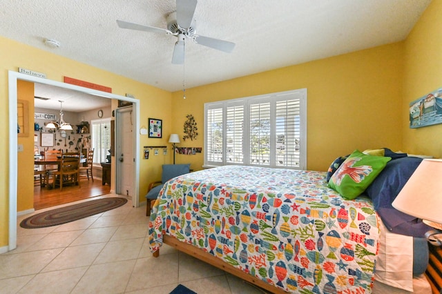 tiled bedroom featuring ceiling fan with notable chandelier and a textured ceiling