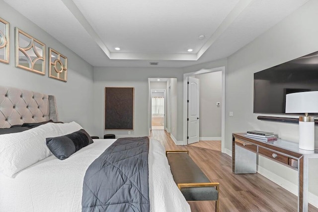 bedroom featuring hardwood / wood-style flooring, a tray ceiling, and connected bathroom