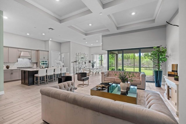 living room with light hardwood / wood-style floors, a high ceiling, beam ceiling, crown molding, and coffered ceiling