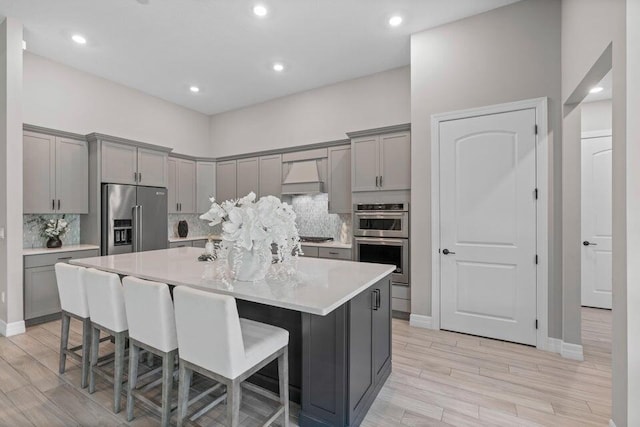 kitchen featuring gray cabinetry, stainless steel appliances, light wood-type flooring, an island with sink, and a breakfast bar