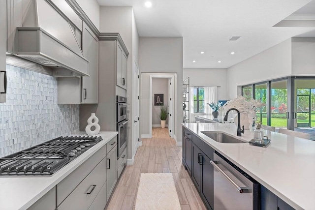 kitchen with gray cabinetry, premium range hood, light wood-type flooring, appliances with stainless steel finishes, and sink