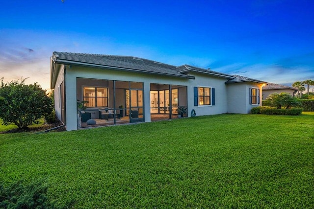 back house at dusk with a patio area, a sunroom, and a yard