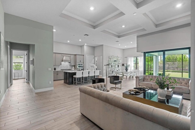 living room featuring light hardwood / wood-style floors, coffered ceiling, ornamental molding, beamed ceiling, and a high ceiling