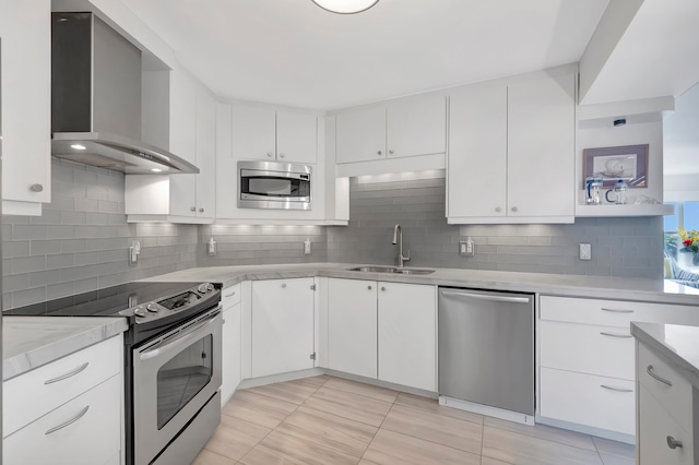 kitchen featuring sink, wall chimney range hood, decorative backsplash, white cabinets, and appliances with stainless steel finishes