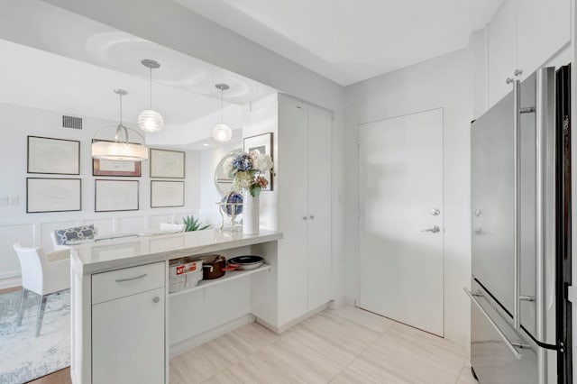 kitchen with kitchen peninsula, decorative light fixtures, white cabinetry, and stainless steel refrigerator