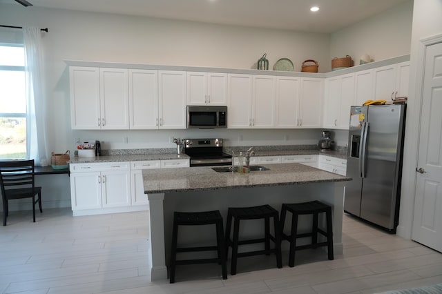 kitchen featuring appliances with stainless steel finishes, a kitchen breakfast bar, sink, a center island with sink, and white cabinetry