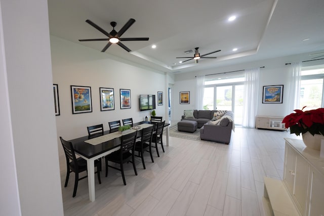 dining area with ceiling fan, a healthy amount of sunlight, a raised ceiling, and light wood-type flooring