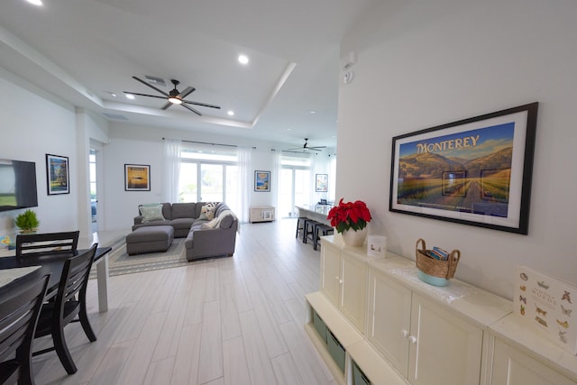 living room featuring a tray ceiling, ceiling fan, and light hardwood / wood-style floors