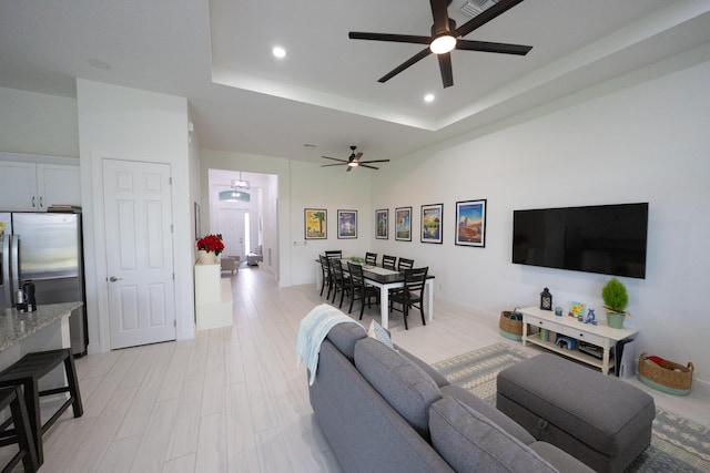 living room with light wood-type flooring, a tray ceiling, and ceiling fan