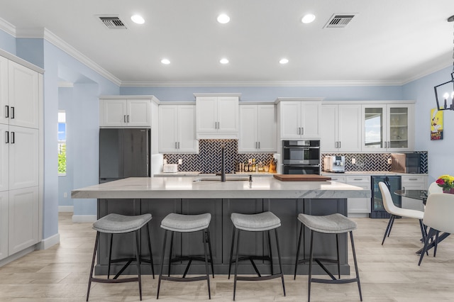 kitchen featuring beverage cooler, sink, an island with sink, and white cabinets