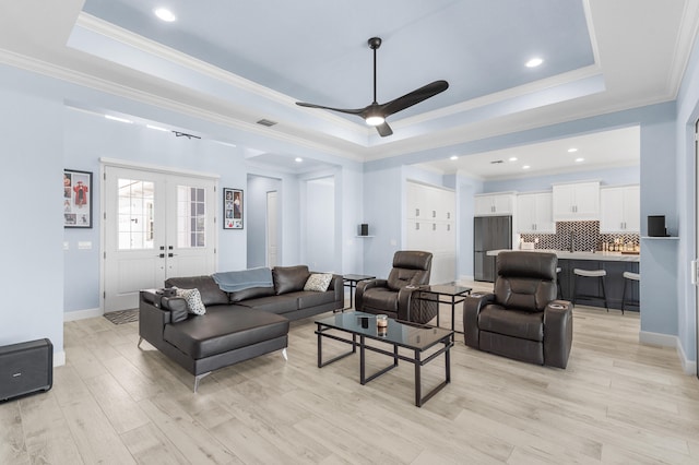 living room featuring light hardwood / wood-style floors, ceiling fan, crown molding, and a tray ceiling