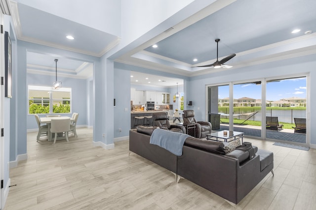 living room with ceiling fan, a raised ceiling, and light wood-type flooring