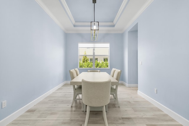 dining area with ornamental molding, a chandelier, light hardwood / wood-style floors, and a raised ceiling