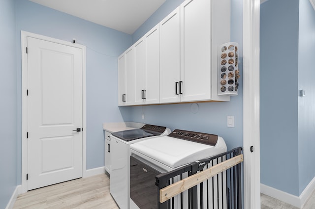 clothes washing area with separate washer and dryer, light hardwood / wood-style flooring, and cabinets