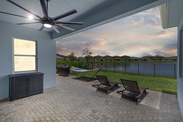 patio terrace at dusk with a lawn, ceiling fan, and a water view