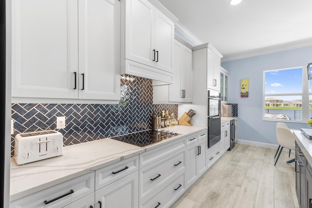 kitchen with crown molding, backsplash, light stone countertops, white cabinets, and light hardwood / wood-style flooring