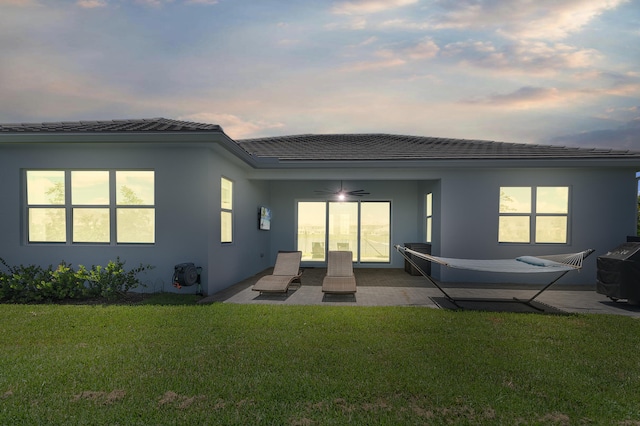 back house at dusk with a patio area, a lawn, and ceiling fan