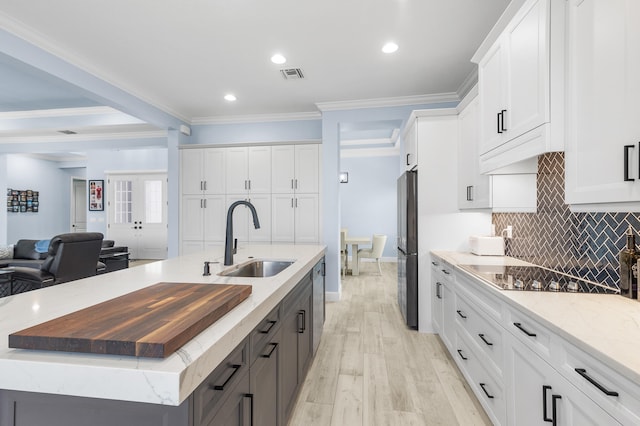 kitchen featuring ornamental molding, a center island with sink, white cabinetry, light wood-type flooring, and sink