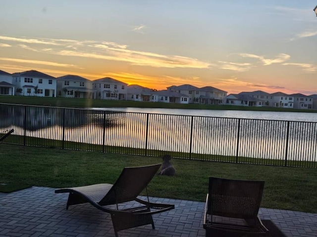 yard at dusk featuring a water view and a patio area