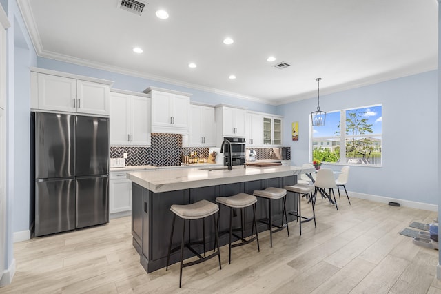 kitchen with white cabinets, stainless steel fridge, an island with sink, and decorative light fixtures