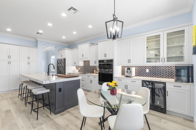 kitchen with stainless steel appliances, white cabinetry, decorative light fixtures, an island with sink, and light hardwood / wood-style floors