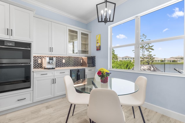 dining room featuring light hardwood / wood-style floors, a water view, beverage cooler, a notable chandelier, and crown molding