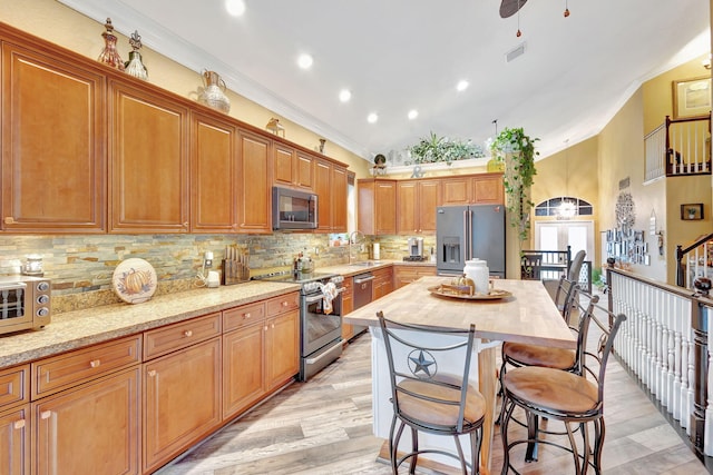 kitchen with light wood-type flooring, stainless steel appliances, ceiling fan, crown molding, and a kitchen island