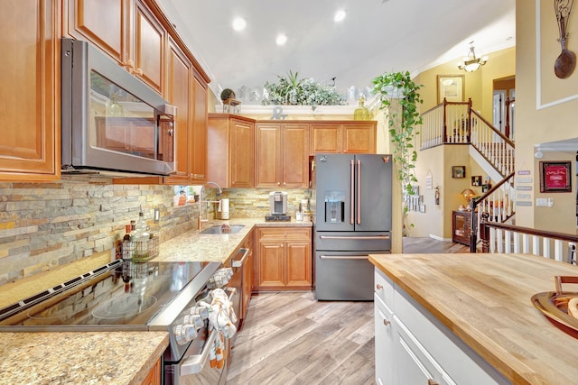 kitchen with appliances with stainless steel finishes, light wood-type flooring, sink, butcher block counters, and lofted ceiling