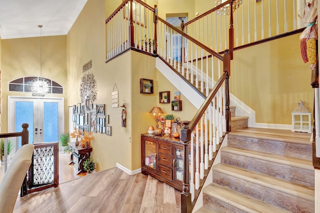 staircase featuring wood-type flooring, crown molding, a high ceiling, and french doors