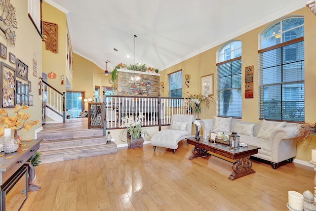 living room with ceiling fan with notable chandelier, crown molding, high vaulted ceiling, and light hardwood / wood-style flooring