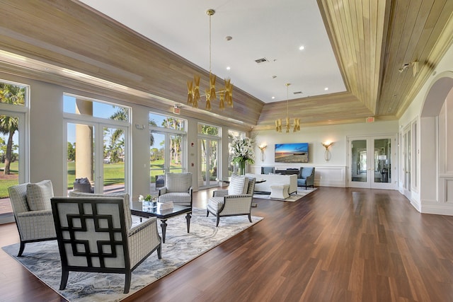 living room with french doors, dark wood-type flooring, a high ceiling, a chandelier, and a tray ceiling