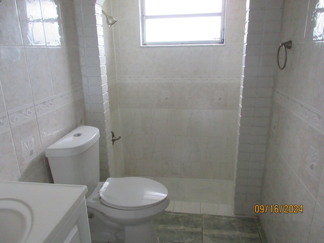 bathroom featuring vanity, toilet, a tile shower, and tile walls