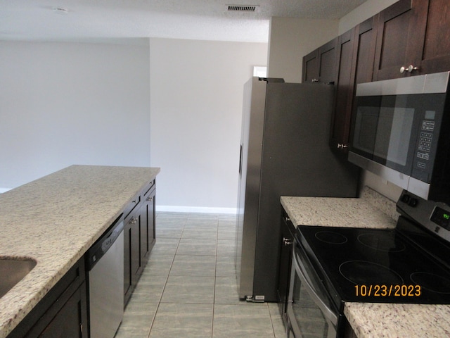 kitchen featuring dark brown cabinetry, light stone counters, appliances with stainless steel finishes, a textured ceiling, and light tile patterned floors