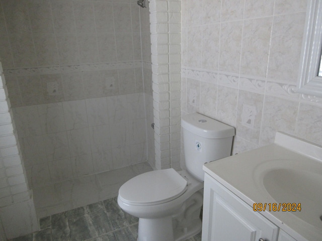 bathroom featuring toilet, vanity, tile walls, and a tile shower