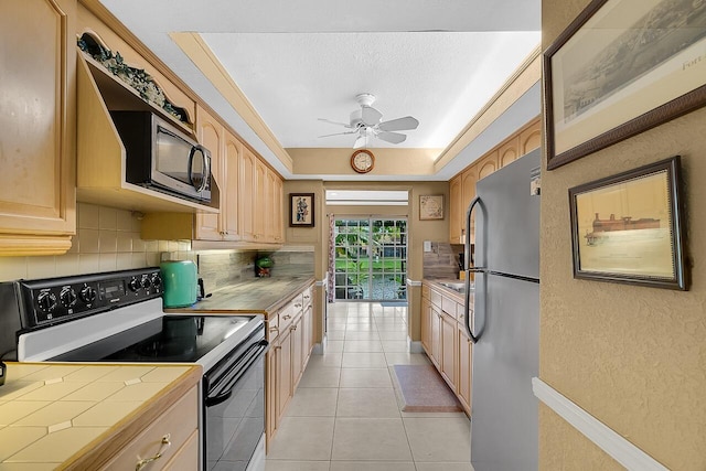 kitchen featuring tile countertops, light brown cabinets, decorative backsplash, ceiling fan, and stainless steel appliances