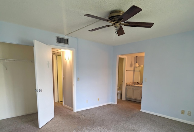 unfurnished bedroom featuring ensuite bathroom, a textured ceiling, light carpet, and ceiling fan