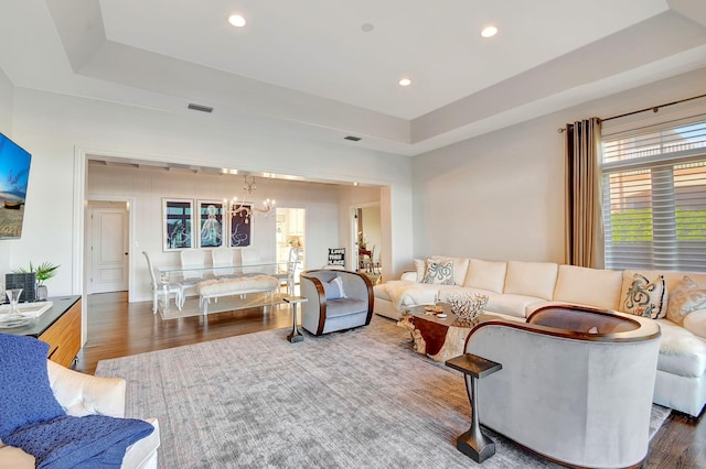 living room with a notable chandelier, a raised ceiling, and dark hardwood / wood-style floors