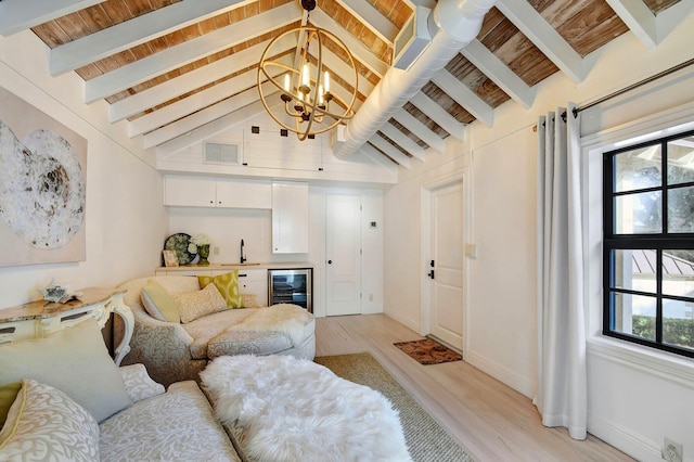 living room with beverage cooler, beamed ceiling, an inviting chandelier, light hardwood / wood-style floors, and wet bar