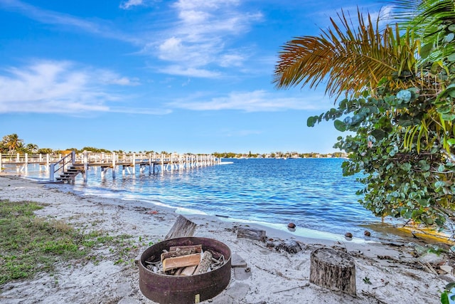 view of dock featuring a water view, an outdoor fire pit, and a beach view