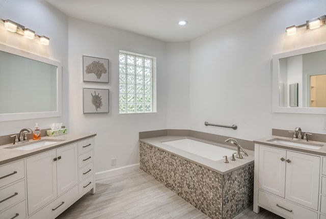 bathroom with hardwood / wood-style flooring, vanity, and tiled tub