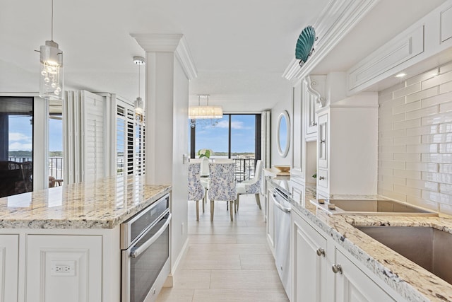 kitchen featuring stainless steel appliances, light stone counters, a chandelier, white cabinetry, and decorative light fixtures